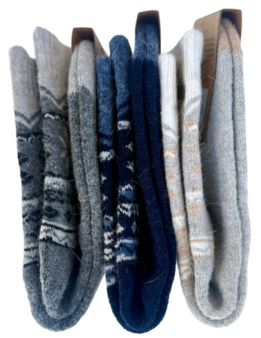 Three pairs of folded knit socks displayed side by side on a white background. The left pair is heather gray with dark gray geometric patterns, the middle pair is navy blue with white geometric patterns, and the right pair is light gray with beige.